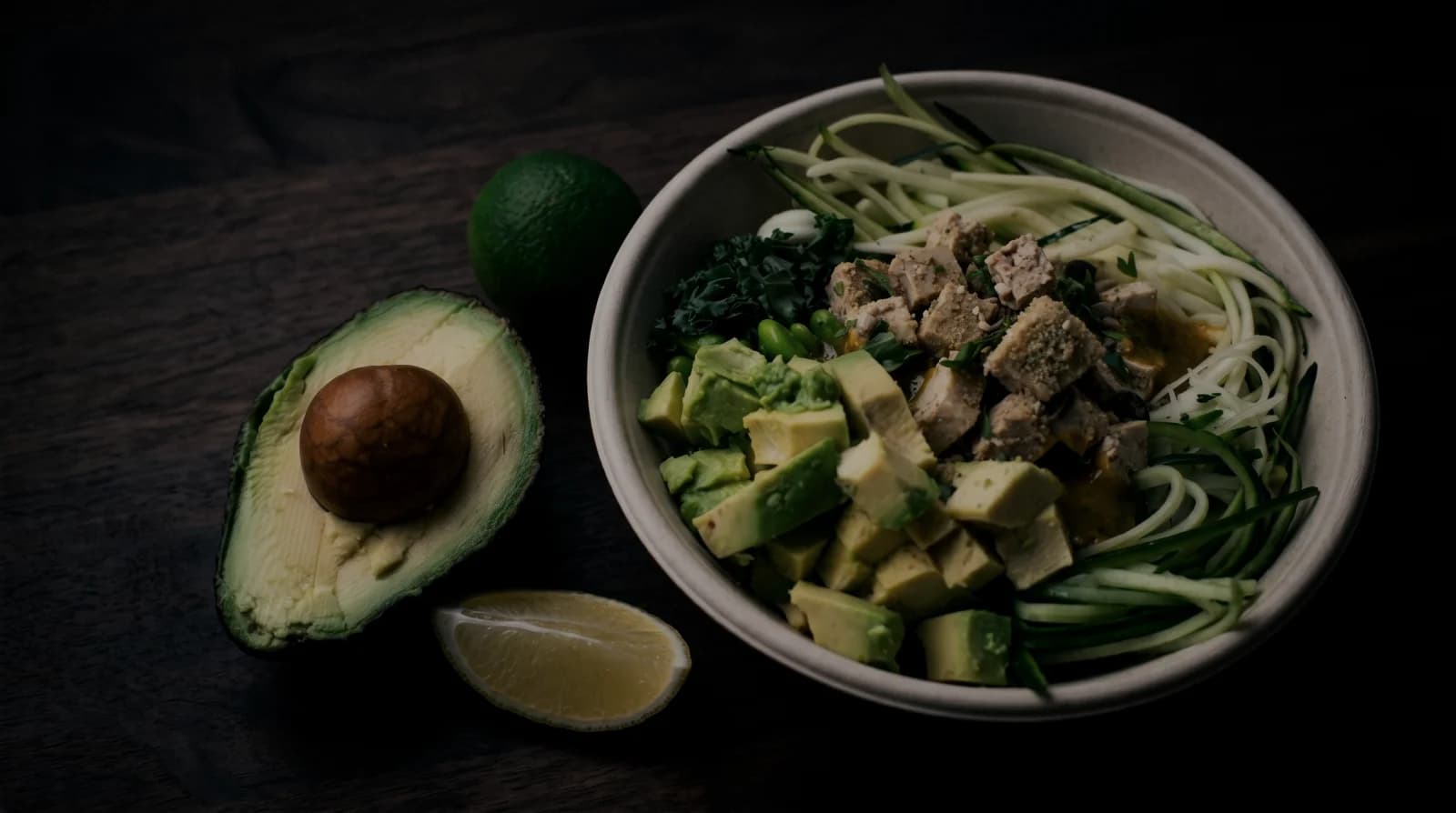 Healthy meal bowl with avocado, greens, and protein on a dark surface
